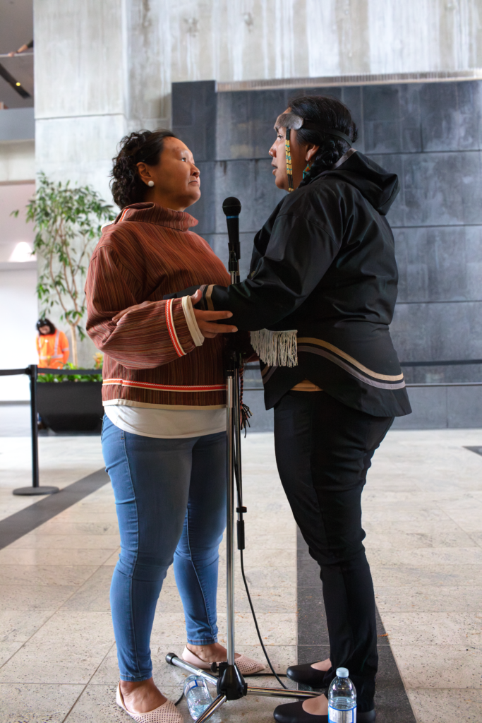 Two Inuit throat singers look into each others faces as they sing.