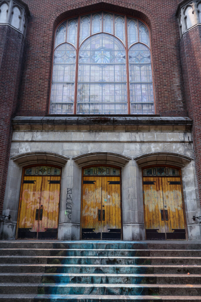 A red brick church with graffiti-worn wooden doors and blue graffiti adorning the steps in Seattle.