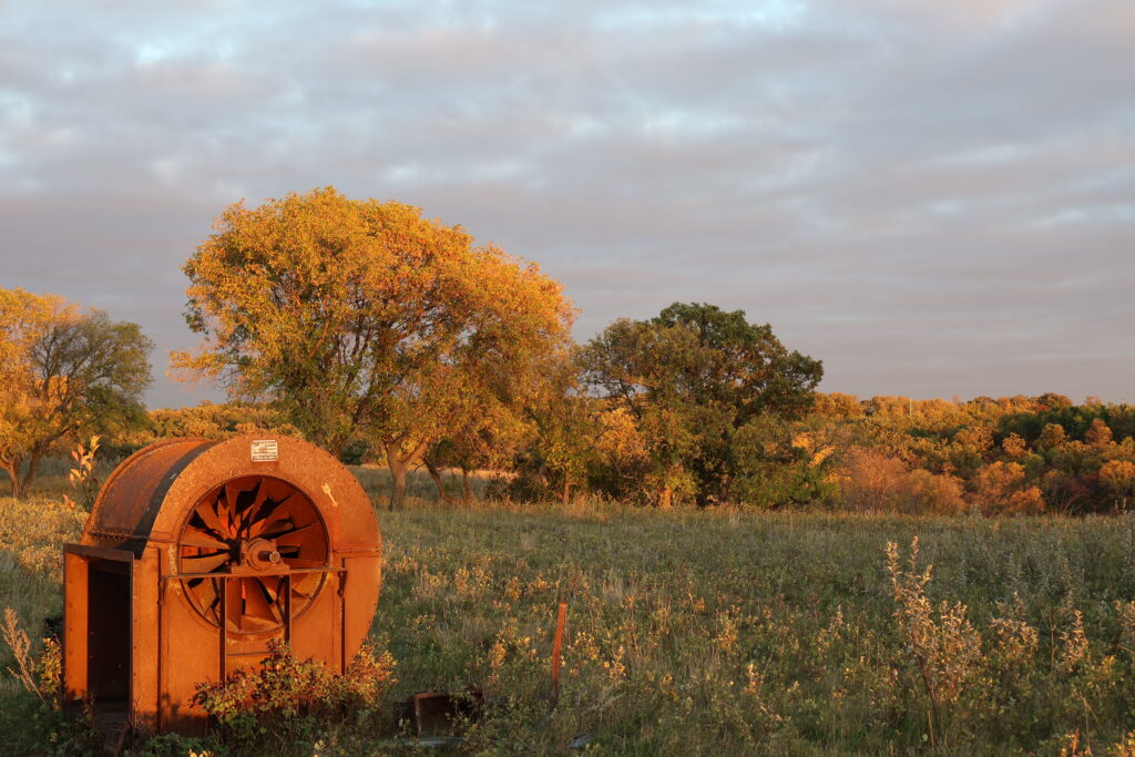Old rusted farm equipment in a field at sunset.